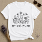 White t-shirt with floral design and text 'Bloom Gently, Grow Wild' on a beige background.