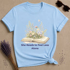 She Reads to Feel Less Alone — Open Book Garden T-Shirt for Women in Light Blue